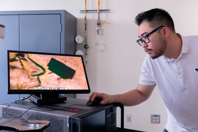 Der Doktorand Zhijian (Chris) Hao mit einem Mikroskopbild eines Mikro-Bots auf einem US-Penny. (Allison Carter, Georgia Tech)