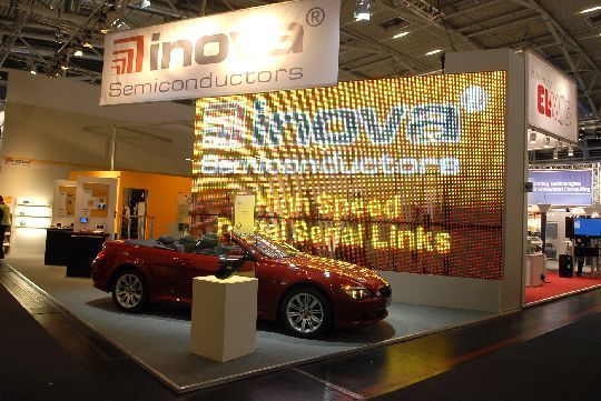 Beispiel zwei erfolgreicher deutscher Chipschmieden: Mit einer eindrucksvollen 4 m x 7 m großen LED-Video-Wand und einem BMW 650 Cabrio hat Inova Semiconductors ihre GigaSTaR- und APIX-Technik präsentiert. Das Müncher Halbleiterunternehmen ist auf die Übertragung von Videodaten im Gigabit-Datenbereich spezialisiert. Das Ausstellungsstück, eine LED-Videowand der Firma G-LEC, besteht aus einzelnen 1x1 m großen Modulen. GigaSTaR ermöglicht die Verteilung der unkomprimierten Videodaten in hoher Qualität. Dabei werden die parallelen RGB-Videosignale in einen digitalen seriellen Videosstrom umgesetzt der eine Datenübertragung über optische Kabel bis zu 1.25 GBit/s ermöglicht. Die verzögerungs- und flimmerfreie Übertragung ist die Grundlage für eine unbegrenzte Verkettung der einzelnen LED-Module. Mit dem BMW-Cabrio wurde  die Anbindung von Headup-Display und Videobildschirm via APIX gezeigt. Inovas High Speed Digital Serial Technik kommt z.B. im neuen BMW 7er serienmäßig zum Einsatz und wird derzeit von Halbleiterunternehmen wie Fujitsu, Toshiba oder Xilinx integriert. (Archiv: Vogel Business Media)