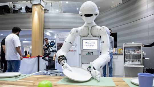Der Roboter ARMAR-7 des Karlsruher Institut für Technologie (KIT) greift vorsichtig einen Teller, um ihn den Geschirrspüler einzuräumen. Er ist insbesondere mit einer kognitiven Architektur mit einem episodischem Gedächtnis ausgestattet, um seine Erfahrungen zu speichern, abzurufen und zu teilen.(Bild:  DLR (CC BY-NC-ND 3.0))