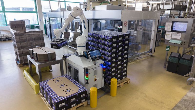 Der Cobot entnimmt die Trays aus dem vorgeschalteten Packer, setzt sie  auf Paletten um und fügt selbstständig Karton-Zwischenlagen ein. (Bild:  Yaskawa Europe GmbH)