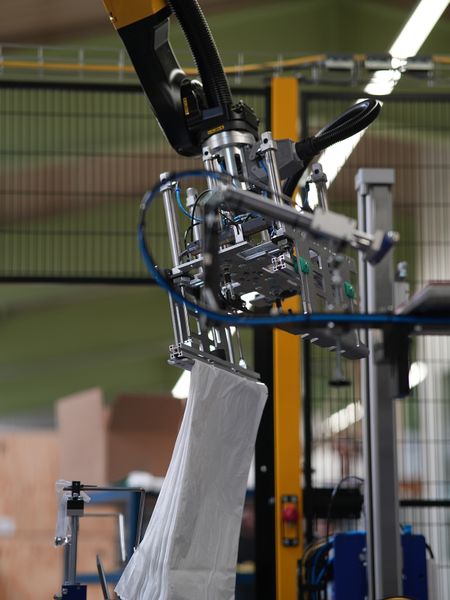 Bild b): Die Bilder a) bis e) zeigen den Transport eines Beutelstapels vom Ablageort über das Anbringen von Pappe und Stopfen sowie das Verschuppen des Bügels bis zur Ablage in den Karton. (Bild: Bihl+Wiedemann)