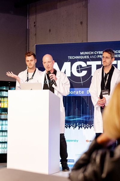 Etwas ganz Besonderes hat sich das Team von TNG einfallen lassen! Martin Förtsch, Thomas Endres und Jonas Mayer zeigten eindrucksvoll, wie KI und Deepfakes u.a. in Videocalls Einzug gehalten haben. (Bild: Vogel IT-Akademie)