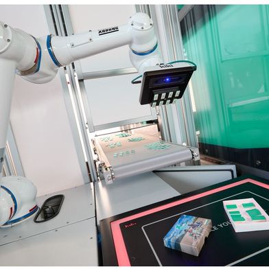 Nachdem ein linearer Multilift V 30 je 32 Dominosteine auf ein Förderband abgelegt hat, übernimmt ein Cobot die nachfolgende Verpackung zum kompletten Domino-Set „ready to use“. (Bild: Arburg)