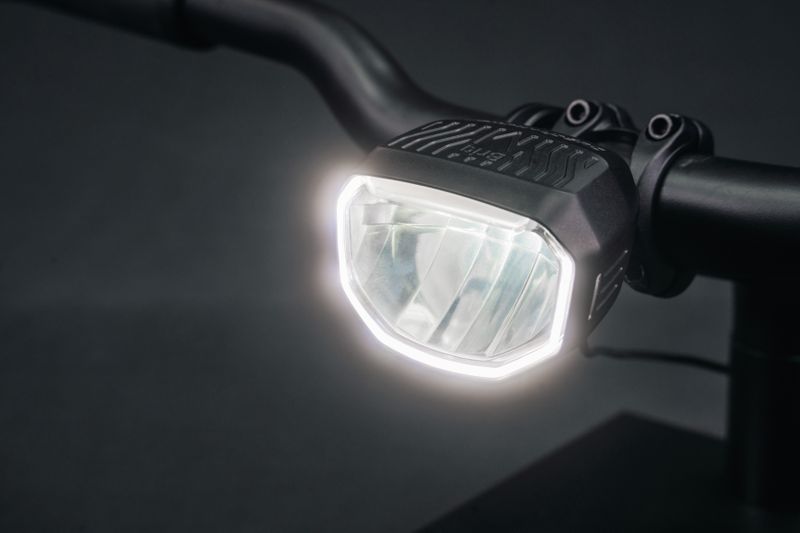 Mit dem „Briq-M E Highbeam“ erweitert Busch + Müller die Briq-Serie um ein kompaktes, leistungsstarkes Fahrradfrontlicht mit Fernlichtfunktion. Im Abblendlicht erzeugt das Modell ein breites und gleichmäßiges Lichtfeld mit einer Beleuchtungsstärke von 150 Lux. Im Fernlichtmodus strahlt der Scheinwerfer mit 200 Lux über die Hell-Dunkel-Grenze hinaus, was insbesondere auf dunklen Überlandstrecken für eine gute Weitsicht sorgt. Der Wechsel zwischen Abblend- und Fernlicht erfolgt via Bluetooth-Verbindung über einen kabellosen Steuerungstaster, der sich entweder über ein Spannband oder eine Aluminiumschelle am Lenker befestigen lässt. Über die hauseigene App können zudem verschiedene voreingestellte Lichtmodi ausgewählt oder individualisiert und die Tastenbelegung verändert werden. Für bessere Sichtbarkeit am Tag verfügt der Scheinwerfer zudem über ein Tagfahrlicht, bei dem der äußere Rand des Scheinwerfers leuchtet. Montiert wird das Licht über eine Kunststoffschelle, die für Lenkerdurchmesser von 31,8 bis 35 Millimeter ausgelegt ist. Der Scheinwerfer erfüllt die Vorgaben der StVZO und eignet sich besonders für schnelle Fahrten auf unbeleuchteten Strecken. Für die unverbindliche Preisempfehlung von 199,90 Euro ist der Briq-M E im Fachhandel erhältlich.   (Bild: www.bumm.de | pd-f)