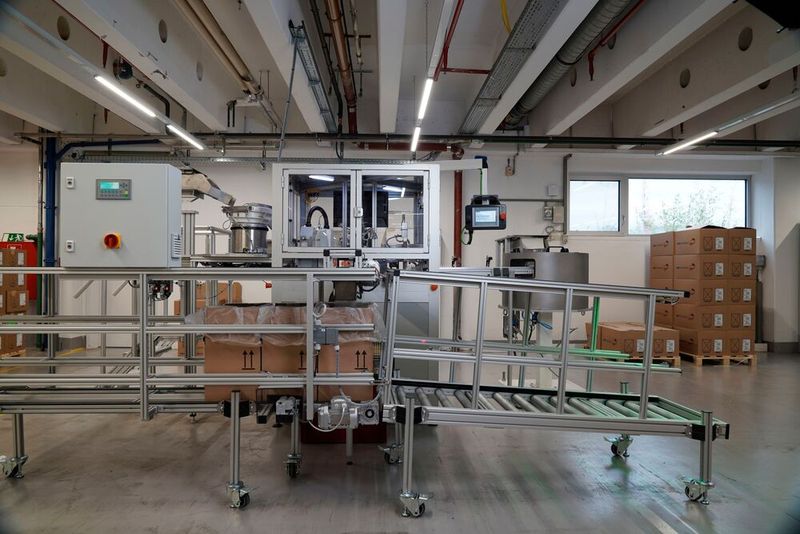 Wenn die Teile in der Rundtaktmontageanlage korrekt montiert wurden, wird das Bauteil zu der Befüllstation transportiert. Dorthin gelangen leere Kartons über Doppelgurtförderer, werden befüllt und anschließend über Rollenbahnen von Item weiterbefördert. (Bild: Item)