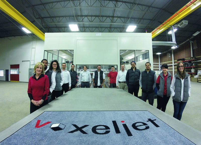 Das Team von voxeljet America steht zum Größenvergleich an der 4000 mm langen Bauplattform - im Hintergrund die VX4000. (Bild: Voxeljet)