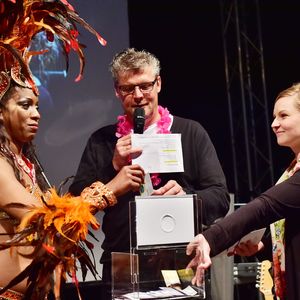 Moderator Norbert Dickel zur Abendveranstaltung mit einer brasilianischen Glücksfee sowie Produktmanagement-Mitarbeiterin Maxi Emmrich (re.)