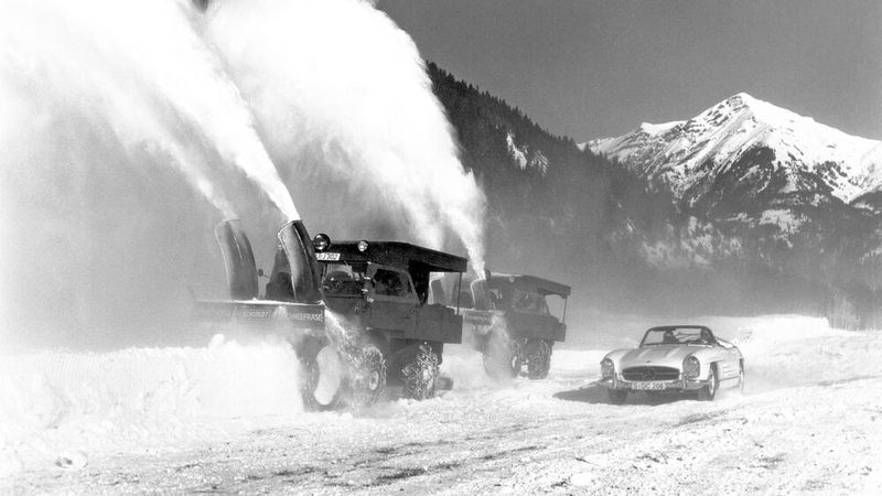 Zwei Mercedes-Benz Unimog der Baureihe 411 mit Schneefräse, angetrieben von einem zusätzlichen Motor auf der Pritsche. Im Vordergrund ein Mercedes-Benz 300 SL Roadster (W 198). Interessant auch die zusätzlich angebrachten „Überdachungen“ über den beiden Fahrzeugen. (Bild: Daimler Truck)