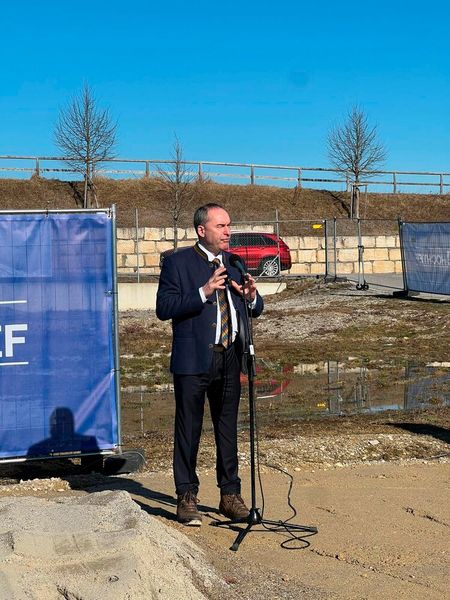 Hubert Aiwanger (Freie Wähler) warnt scherzhaft davor, dass der Baustart verschoben werden müsse, falls sich aus der Pfütze vor Ort ein Biotop bilde. (Bild: Paula Breukel)