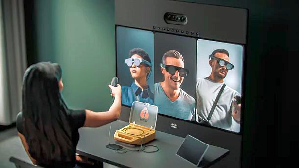 Die Cisco Webex Hologram Machine dient der Bilderfassung und -übertragung, aber auch der Empfänger braucht neben der VR-Brille offenbar eine Art Projektor oder einen Webex-Monitor (Desk Pro & Kamera). In der Hand hält die Empfängerin eine Art Lichtzeiger. (Bild: © Cisco - Matzer)