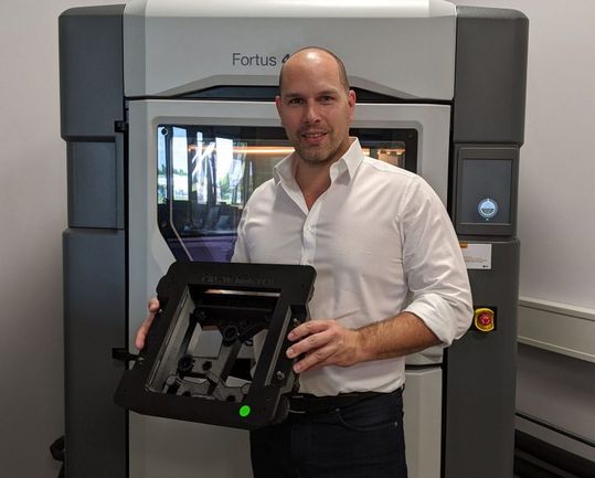(Stefan Kammann vor dem Fortus 450mc 3D-Drucker im ADaM Competence Center mit einer 3D-gedruckten, ESD-konformen Klebevorrichtung. Bildquelle: Continental AG)