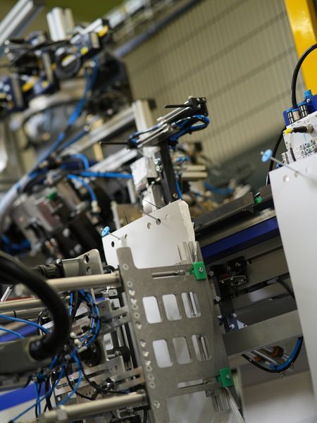 Bild c): Die Bilder a) bis e) zeigen den Transport eines Beutelstapels vom Ablageort über das Anbringen von Pappe und Stopfen sowie das Verschuppen des Bügels bis zur Ablage in den Karton. (Bild: Bihl+Wiedemann)