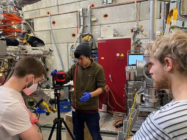 Die drei Doktoranden (v.l.) Robert Waddy, Jesse Zhang und Paul Wegmann richten das Experiment auf die Strahlführung aus. (Bild: Anna Soter / ETH Zürich)