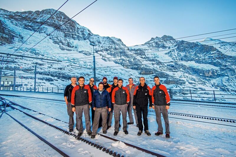 L'équipe des ateliers du glacier de l'Eiger, et la vue imprenable de leur lieu de travail. (Thomas Entzeroth)