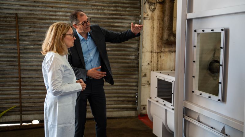 US-Unternehmerin Nancy Sanders und Geschäftsführer Herwig Thiel vor dem Kunststoffzerkleinerer der Pilotanlage RewinPlast. (Bild:  RewinPlast)