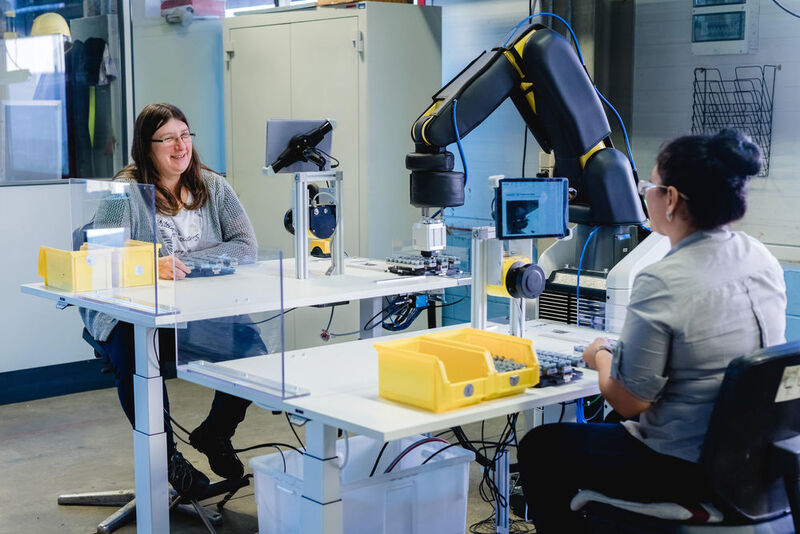 Der im Projekt Aquias entwickelte Arbeitsplatz für Mensch-Roboter-Kollaboration im Überblick: Die Tische sind je nach Bedarf individuell höhenverstellbar, der Roboter arbeitet den Mitarbeitern von der Seite zu, die Mitarbeitenden sitzen sich gegenüber und können miteinander kommunizieren. (Ludmilla Parsyak/ Fraunhofer IAO)