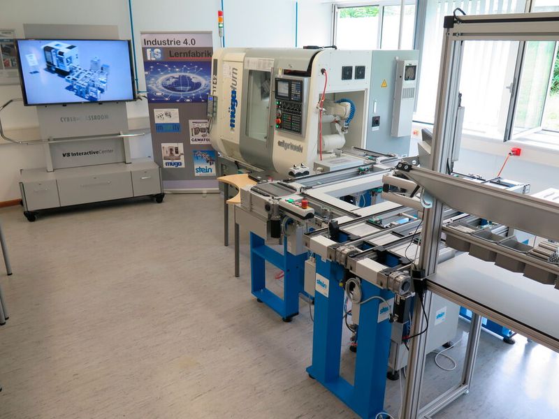 Blick auf die Anlage der Lernfabrik mit Handarbeitsplatz (r.), Transportsystem des Werkzeugträgers und Bearbeitungszentrum mit Roboter. Im Hintergrund links der Bildschirmaufbau für den Cyber-Classroom. (Bild: Feintechnikschule Schwenningen)