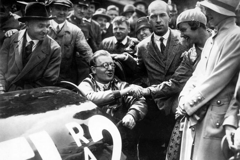 Im Ziel: Fritz von Opel nimmt Glückwünsche von der Motorrad-Rennfahrerin Hanni Köhler entgegen. Neben ihr blickt Max Valier mit erstem Blick in die Kamera. Ganz links Opel-Rennfahrerlegende Carl Jörns, rechts im Vordergrund Lilian Harvey. (Opel)