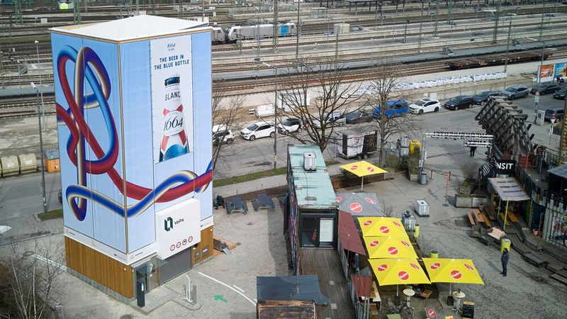 The vertical parking tower near Munich's Ostbahnhof is clad with wooden elements. Some surfaces are used for advertising banners, while others were artistically designed (design by Mariella Kerscher).(Image: Vepa Vertical Parking)