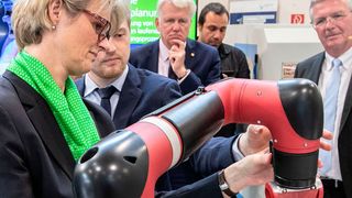 Lukas Nikelowski (Fraunhofer-IML) hilft Ministerin Karliczek bei der Bedienung eines Roboterarms. Im Hintergrund (v.l.): Prof. Dr. Georg Rosenfeld, Ullrich Sierau, Georgios Katsimitsoulias und Prof. Dr. Michael ten Hompel. (Fraunhofer-IML)
