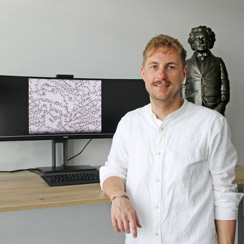 Prof. Dr. Christopher Kuenneth, Universität Bayreuth. Der Bildschirm zeigt die atomistische Struktur eines Polymers mit Kohlenstoff-Atomen (graue Kugeln) und Wasserstoff-Atomen (weiße Kugeln). 