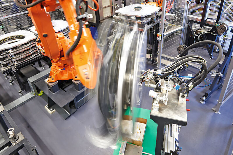 Roboter mit schnell drehender Montagehilfe beim Auftragen des Klebstoffes auf die in der Montagehilfe eingelegten Magnetschalen. (Thyssenkrupp)