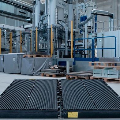 Die beiden schwarzen Bauteile vor dieser Wickert-Presse haben bewiesen, dass man leichte Batteriegehäuse für die E-Mobilität wirtschaftlich auch aus faserverstärkten Thermoplasten herstellen kann. Das brachte dem Team der TU Chemnitz den JEC Innovation Award 2026 ein. (Bild: TU Chemnitz)