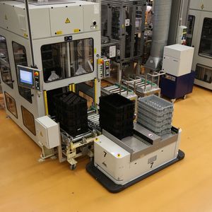 Ein fahrerloses Transportfahrzeug vom Typ Caesar übergibt Trays mit Halbfertigteilen zur weiteren Bearbeitung an eine Produktionsmaschine.(Bild:  MLR Gruppe)