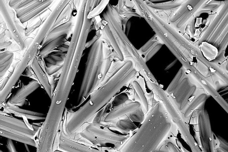 Ein neues Wettbewerbsprodukt unter dem Elektronenmikroskop: Deutlich sichtbar ist die auf die Filterfasern aufgebrachte Beschichtung mit beginnender Rissbildung. (UFI)