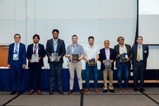 Six of the seven authors accept their NAMRC Outstanding Paper award on June 17, 2026. At the far left and far right are conference officials Xun Xu and Brett Conner. Holding the plaques are (left to right) authors Shivam Garg, Aryan Shroff, Ricardo Toro, Jorge E. Correa, Shiv G. Kapoor, and Placid M. Ferreira. Co-author Liang Tung Chen was not present.(Source:  Jason / Grainger College of Engineering at the University of Illinois Urbana-Champaign)