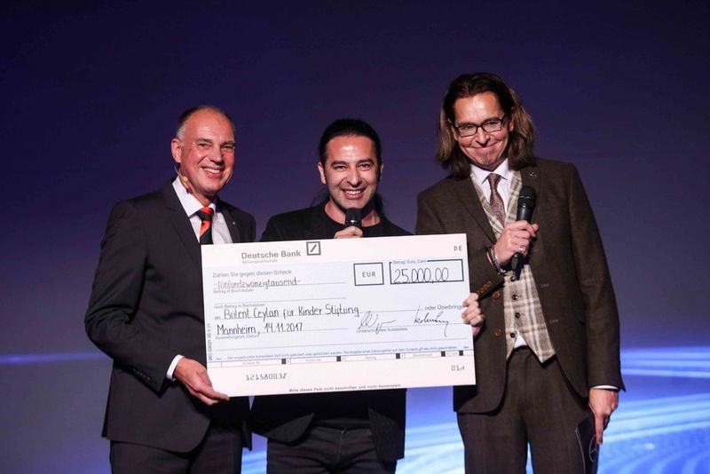 Im Rahmen der Neueröffnung überreichte Mercedes-Benz Pkw Verkaufsleiter Andreas Koltermann (l.) einen Scheck über 25.000 Euro an den Mannheimer Comedian Bülent Ceylan für dessen „Bülent Ceylan für Kinder“-Stiftung. Sein Kollege Christian „Chako“ Habekost (r.) freute sich mit ihm.  (Daimler AG)