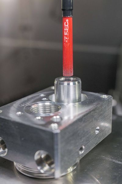 Rechter Ausbruch am Bohrungsgrund: die Tieflochbohrung endet halboffen in der Bodenfläche und im Freistich entsteht ein Grat, der nur durch den Einsatz der Keramikfaser Cross-Hole Bürste Typ Bücha127M entgratet werden kann. Unter Drehzahl spreizen sich bei diesem Bürsten-Typ die einzelnen Fasern durch die Fliehkraft auf und entfernen somit sanft entstehende Mikro-Grate.  (Bild: Kempf)