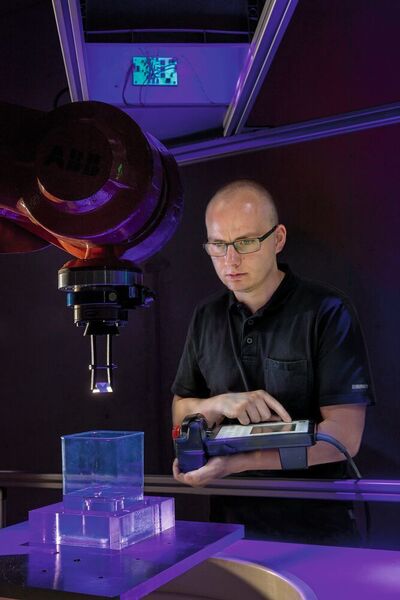 Max Schneckenburger, Masterand Maschinenbau, glättet die Oberfläche einer 3D-gedruckten Kunststoffoptik mit dem Robot-Dip-Coating-Verfahren. Dabei wird die Acrylat-Optik in ein Harzbad getaucht und unter UV-Licht ausgehärtet. (© Thomas Klink, Hochschule Aalen)