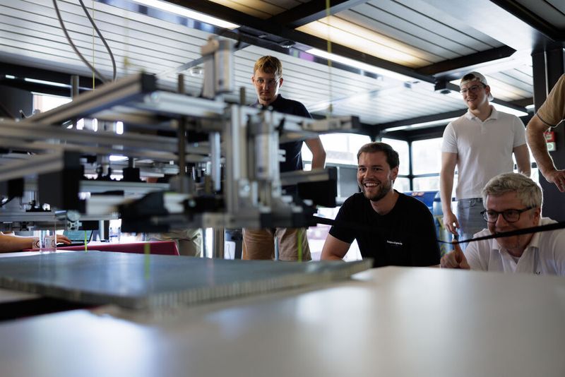 Marco Deffner von Beyond Gravity (z. v. l.) betrachtet einen funktionierenden Prototyp, der eine hochempfindliche Aluminium-Wabenstruktur für Raketenverkleidungen automatisch transportiert. (Bild: Cyrill Maag)