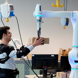 Forscher Federica Masiero nimmt ein Päckchen entgegen, dessen Gewicht der Roboter vorher bereits an das Exoskelett übermittelt hat. (Bild:  Andreas Schmitz / TUM)