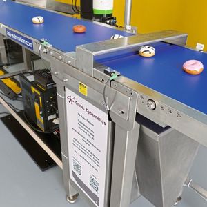 An der ersten Bildverarbeitungsstation reicht ein ganz schmaler Spalt zwischen zwei Transportbändern aus, um die Donuts mit einem 3D-Profilsensor der Z-Trak-2-Serie von Teledyne Dalsa auf Fehler an der Unterseite zu überprüfen. (Bild:  Teledyne Dalsa)