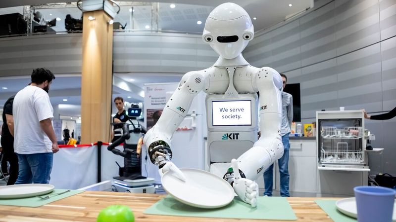 Der Roboter ARMAR-7 des Karlsruher Institut für Technologie (KIT) greift vorsichtig einen Teller, um ihn den Geschirrspüler einzuräumen. Er ist insbesondere mit einer kognitiven Architektur mit einem episodischem Gedächtnis ausgestattet, um seine Erfahrungen zu speichern, abzurufen und zu teilen.  (Bild: DLR (CC BY-NC-ND 3.0))