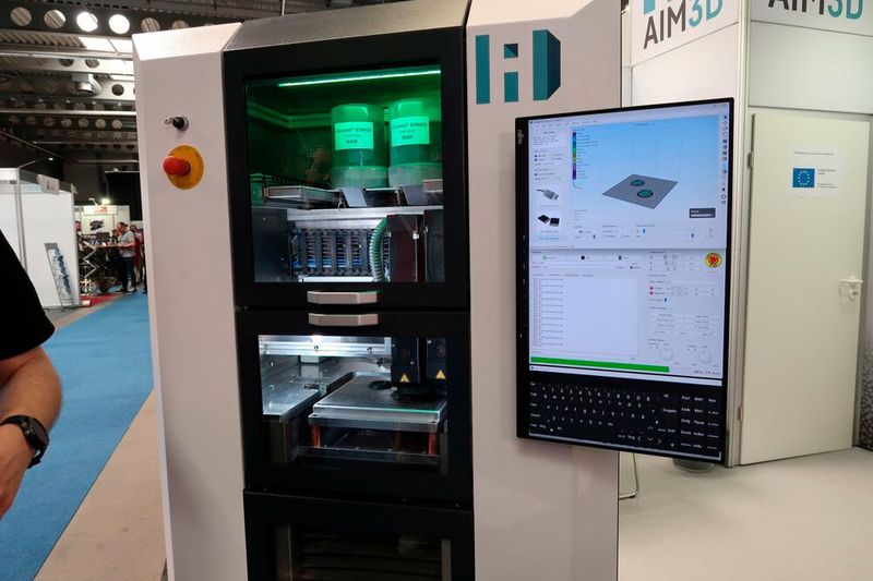 AIM3D zeigte seinen Multimaterial-3D-Drucker ExAM 255. Das zugrunde liegende Composite Extrusion Modeling (CEM-Verfahren) kombiniert den Metallspritzguss, den Keramikspritzguss und den eigentlichen Spritzguss mit dem FDM-Verfahren. So können auf Grundlage von Standard-Spritzgussgranulaten Produkte aus Metallen, Keramiken, Kunststoffen und verstärkten Kunststoffen additiv entstehen. (Bild: D. Quitter - VCG)