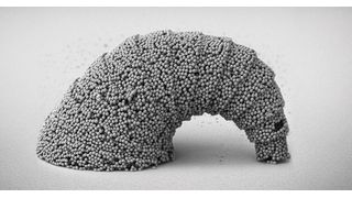 Rasterelektronenmikroskopische Aufnahme einer hängenden, croissantförmigen Mikrostruktur mit einer 3D-gekrümmten Oberfläche, die aus SiO2-Partikeln zusammengesetzt ist. (Bild: MPI-IS)