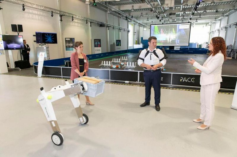 Bundesarbeitsminister Heil am Fraunhofer-Institut für Materialfluss und Logistik IML mit körperentlastendem Exoskelett, das dort getestet wird. Im Vordergrund der AMR „evoBOT“. (Bild: Fraunhofer IML)