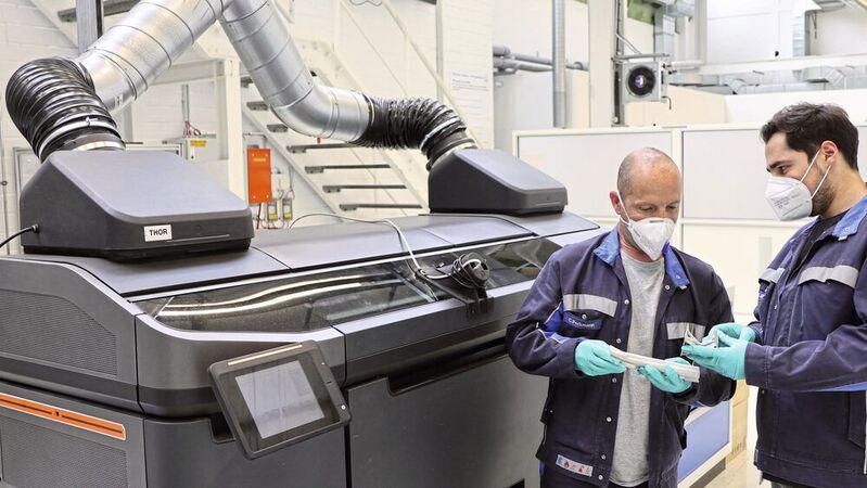 Zwei VW-Mitarbeiter prüfen die Qualität von im Binder-Jetting-Verfahren hergestellten Strukturteilen vor dem Prototyp des Spezialdruckers im Wolfsburger 3D-Druck-Zentrum.