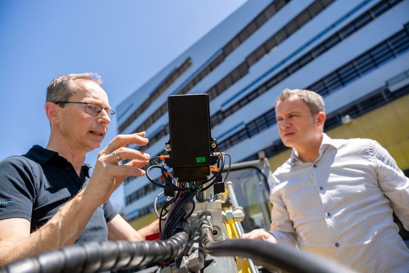 Andreas Plöckinger und RWT-Vorstand Reinhard Thor (v.l.) begutachten das CPS-Ventil am Löffelstiel eines Baggers. Im Hintergrund der LCM-Firmensitz im Linzer Science Park. (Bild: Pecksteiner/LCM)