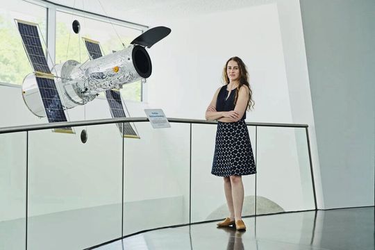 Prof. Dr. Laura Kreidberg steht neben einem Modell des Hubble- Weltraumteleskops im Maßstab 1:10. Bevor das James-Webb-Weltraumteleskop die Arbeit aufnahm, war dies das leistungsstärkste Auge im All.(Bild:  Anna Ziegler für MPG)