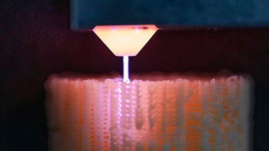 Beim Fused Deposition Modeling (FDM) sind inhomogene Fertigkeitswerte in Z-Richtung eine potenzielle Schwachstelle. Abhilfe kann eine Plasmabehandlung während des Bauprozesses schaffen. Das Fraunhofer IST entwickelt nun eine Ring-Plasmaquelle, die um die Düse des 3D-Druckers montiert werden kann.(Bild:  Fraunhofer IST /  Paul Kurze)