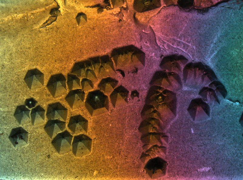 Wachstumsstrukturen (Negativkristalle) in Aquamarin (Varität von Beryll). Fundort: Tansania. Das Wachstum von Beryllkristallen ist in der Regel viel schneller in Richtung der Längsachse des Kristalls als quer dazu. Somit führen bereits geringe Unregelmässigkeiten im Kristall zur Bildung von gelängten Hohlkanälen, die im weitern Verlauf langsam teilweise verheilen und durch Kristallflächen begrenzt sind (so genannte Negativkristalle). Im vorliegenden Bild handelt es sich bei den Negativkristallen um sechsseitige Pyramiden, die sich auf einer früheren Kristalloberfläche gebildet haben. Bildbreite: ca. 4 mm, Auflicht (Glasfaserbeleuchtung) im Dunkelfeld, einfach polarisiertes Licht (Analysator), Leica MZ16 Stereomikroskop (Michael Hügi, Schweizerisches Gemmologisches Institut)