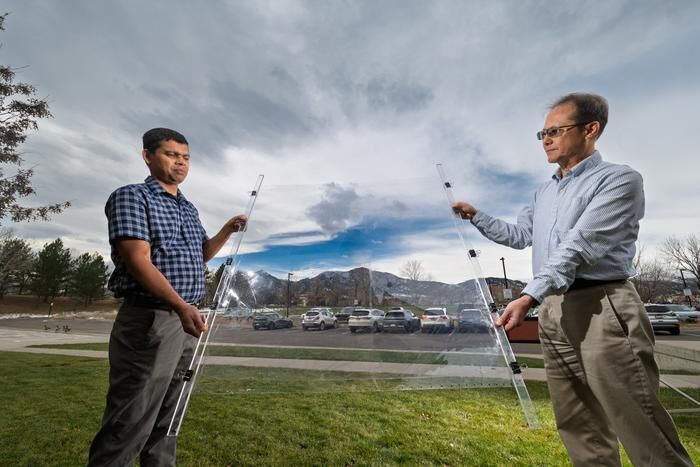 Eldho Abraham, left, and Taewoo Lee, right, hold up a new window insulation material called Mochi-affixed to a thin sheet of plastic, which was designed by CU Boulder researchers in physic professor Ivan Smalyukh’s lab.  (Source: Glenn J. Asakawa/CU Boulder)