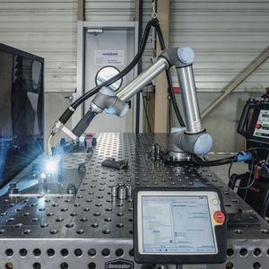 Dank der Reichweite von 1,3 m kann der Cobot zwei Vorrichtungen auf einem Schweisstisch bedienen. Währenddessen bereitet ein Mitarbeiter hinter einer Sichtschutzwand schon den nächsten Auftrag vor. 