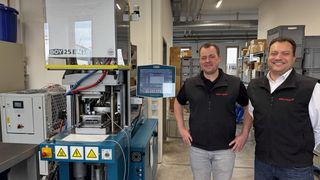 Philipp Geiges (rechts), Geschäftsführer der Werner Sauter GmbH, und Dominik Geiges, technischer Leiter und Prokurist, vor der Vertikalspritzgießmaschine Boy 25 E V H. Auf der kompakten Anlage wird eine Sensorplatine inklusive angelöteter Leitung mit dem Hotmelt-Material Macromelt PA678 von Henkel prozesssicher umspritzt. (Bild: Redaktion/Stefan Lenz)