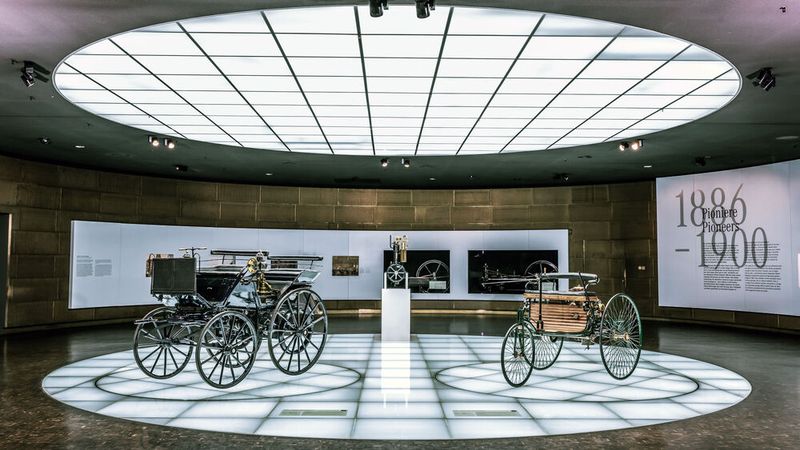 Mercedes-Benz Museum, Stuttgart. Benz Patent-Motorwagen (rechts) und Daimler Motorkutsche (links) im Raum Mythos 1: Pioniere – Die Erfindung des Automobils, 1886 bis 1900. In der Mitte die Daimler „Standuhr“ – der erste kleine, schnelllaufende Verbrennungsmotor. (Bild: Mercedes-Benz AG)