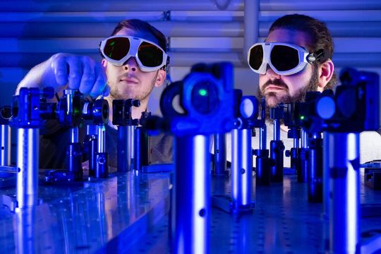 Besser als binär! Von links: Paul Herrmann und Sebastian Klimmer experimentieren an einem Laserversuchsaufbau an der Universität Jena, mit dem untersucht wird, wie man mit Licht und 2D-Materialien Informationen rund 1.000 Mal schneller übermitteln kann als mit Strom.(Bild:  Uni Jena / J. Meyer)